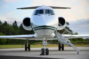 Ein Privatjet von vorne mit ausgefahrener Treppe, geparkt auf einem Rollfeld mit Bäumen und Grün im Hintergrund.