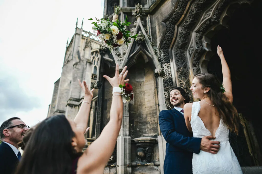 Ein frisch vermähltes Brautpaar mit Gästen vor einer historischen Kirche.